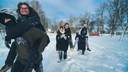 Cheerful schoolgirls enjoying piggyback rides in a snowy park, celebrating winter with playful games and laughter