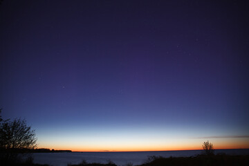 Night clear sky view with starts and late sunset on horizon, sea shore