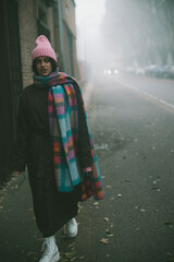 A woman in a pink hat and scarf walks down a foggy street