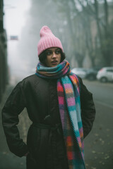 A woman in a pink hat and scarf stands on a foggy street