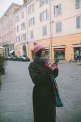 A woman in a pink hat and scarf is intently looking at her phone