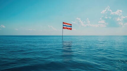 A lone flag stands tall in the vast ocean under a bright blue sky. The serene scene evokes feelings of peace and freedom.