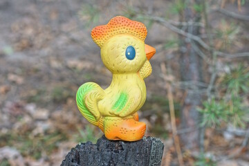 one small colored rubber toy cockerel stands on a black stump on a summer street