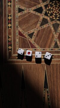 A closeup of white dice, featuring a mix of black and red dots, set on a beautifully crafted traditional backgammon board with intricate Arabic patterns and warm shadows.