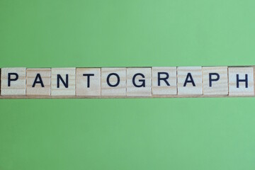 word pantograph made of small gray wooden letters on a green paper background