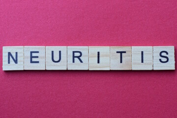word neuritis from gray wooden small letters with black font on an red table
