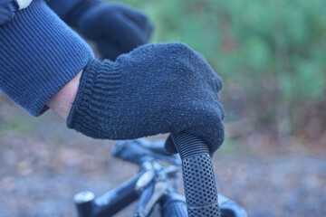 hand of one male cyclist in black wool glove holds plastic handlebar of bicycle on autumn street