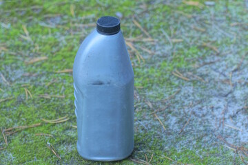 one old gray plastic dirty canister stands on the ground and green moss on a summer street