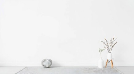 White room with a round white ottoman, two vases with dry branches and a small wooden table.