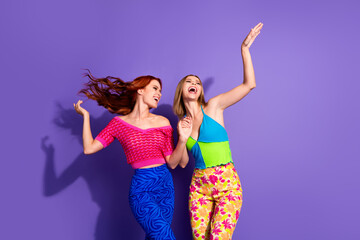 Portrait of two nice stunning girls hold hands dancing chilling isolated on purple color background