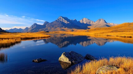 Naklejka premium Serene Lake Reflecting Majestic Mountains Under Clear Blue Sky, Surrounded by Lush Autumn Grass for Nature Lovers and Outdoor Enthusiasts