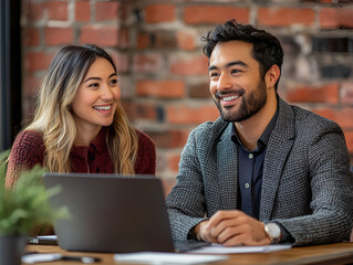 a photo of two business people sitting at a table in an office, working on laptops and smiling at each other while looking into the camera. they are wearing casual and appear professional yet relaxed,