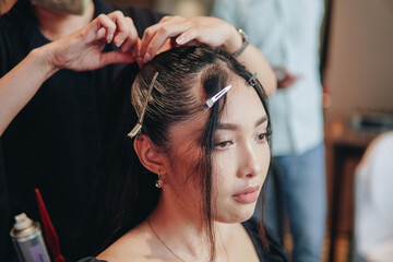 Fototapeta premium Attractive young Asian woman sitting and getting a hairdo by a hairdresser in a beauty salon.