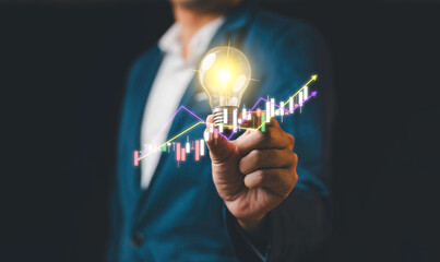 A businessman holding a glowing light bulb with financial graphs and upward trends, symbolizing innovation, success, and business growth.