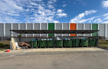 A row of green trash cans are lined up on the side of a road