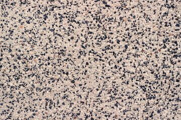 The texture of a mosaic surface with black and white stones evenly distributed on a light base