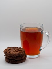 In this inviting image, a glass cup of tea is paired with chocolate cookies and a cluster of fresh red berries, all set against a soft, neutral backdrop conveying warmth.