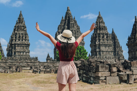 Back portrait of a carefree young Asian woman stands in front of Candi Prambanan temples.