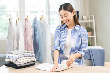 Housewife, happy asian young woman, girl hand folding freshly white shirt on table after washing...
