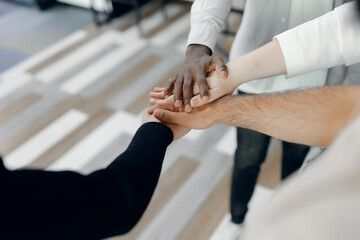 Diverse group joining hands in business environment, symbolizing unity, inclusion, and teamwork...