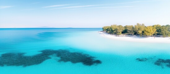 Obraz premium Aerial view of pristine beach with turquoise waters and lush greenery on the shoreline under a clear blue sky