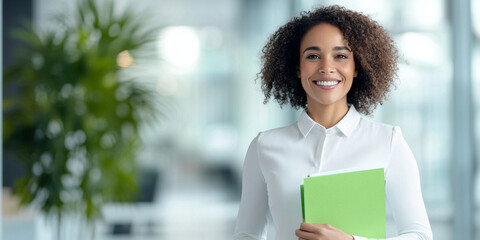 confident woman smiles while holding green folders in modern office. Her curly hair and professional attire reflect positive and productive atmosphere