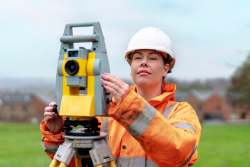 Woman surveying professional checks equipment in a green field setting while wearing safety attire