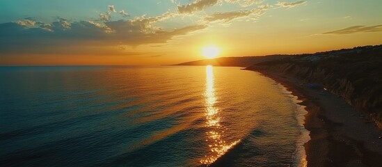 Golden hour sunset reflecting on calm sea shimmering over coastline with serene beach setting ideal for relaxation and tourism