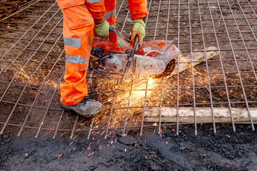 Construction worker using power saw cutting tool on steel rebar at construction site during daytime