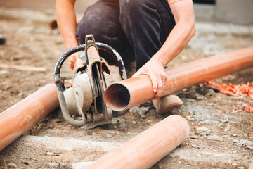 Worker cuts plastic drainage pipes on construction site during daylight hours