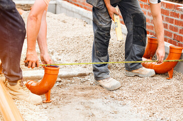 Workers installing plastic drainage pipes on a construction site during daylight