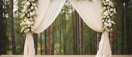 Rustic outdoor wedding arch draped in white fabric and adorned with flowers surrounded by a serene forest backdrop for a picturesque ceremony