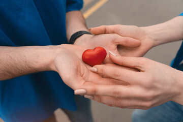 Couple sharing a small red heart shape in their hands during a sunny day in an urban setting