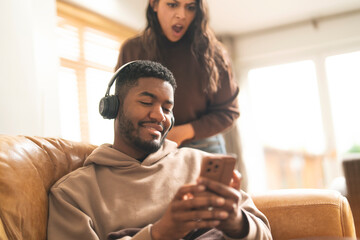 Person enjoying music on a couch while another expresses surprise or frustration in a bright living room