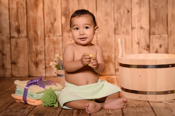 depicts a small child sitting on a wooden floor. He is wrapped in a towel, with accessories around...
