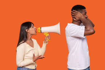 Woman using megaphone to communicate with man ignoring her in front of bright orange background