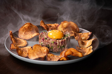 meat hackepeter tartare dish with raw egg yolk and fried sweet potato chips isolated in isolated angle smoked with smoke