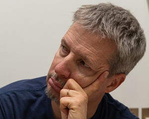 Thoughtful mature man with a contemplative expression, resting his chin on his hand