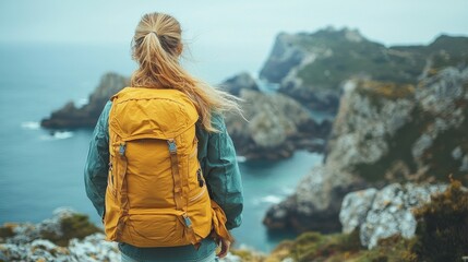 Fototapeta premium Woman with yellow backpack enjoys coastal view on a cloudy day in a rugged landscape