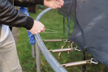 A guy removes springs from a trampoline while disassembling it.