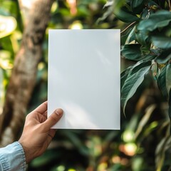 A hand holding a blank sheet of paper amidst lush green foliage and nature