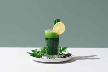 Jugo batido de espinacas adornado con una rodaja de limón sobre mesa blanca y fondo verde