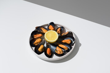 Plato de mejillones al vapor con limón sobre una mesa blanca y fondo gris