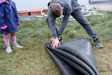 Children take apart a large trampoline at home and reassemble it.