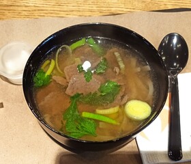Fo-bo. Asian food. Hot soup in a black bowl on a tray. There is a black spoon next to it.