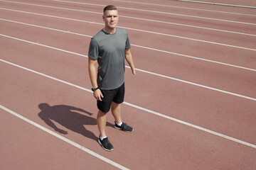 Athlete standing on track field wearing a gray t-shirt and black shorts. Preparing for athletic training outdoors. Shadow casted on running track