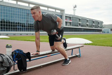 Athletic young man performing arm exercises with dumbbells on outdoor track. Engaging in strength training activities with focus and determination