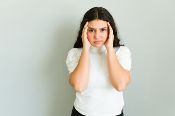 Latin teenager in pain from a migraine, holding her temples in discomfort