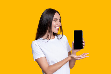 Woman presenting phone screen. Young girl showing phone isolated on yellow. Millennial woman. New phone app. Girl offer advertisement. Presenting product. Advertisement of business app. Work online