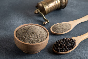 A bowl of black peppercorns on a black background and a metal grinder